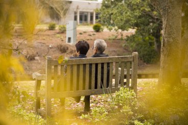 Zwei Senioren sitzen in einem Park auf einer Bank.