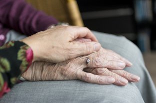 Pflegerin legt ihre Hand auf die verschränkten Hände einer Seniorin